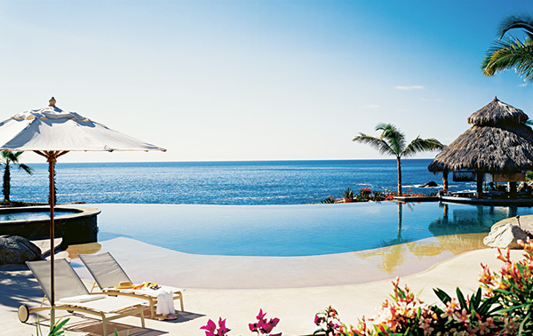 An infinity pool overlooks a glittering ocean view on a clear day.