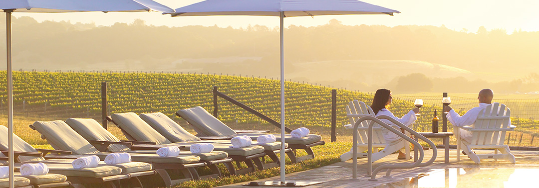 A loving couple sit on lounge chairs and look out over wine vineyards.
