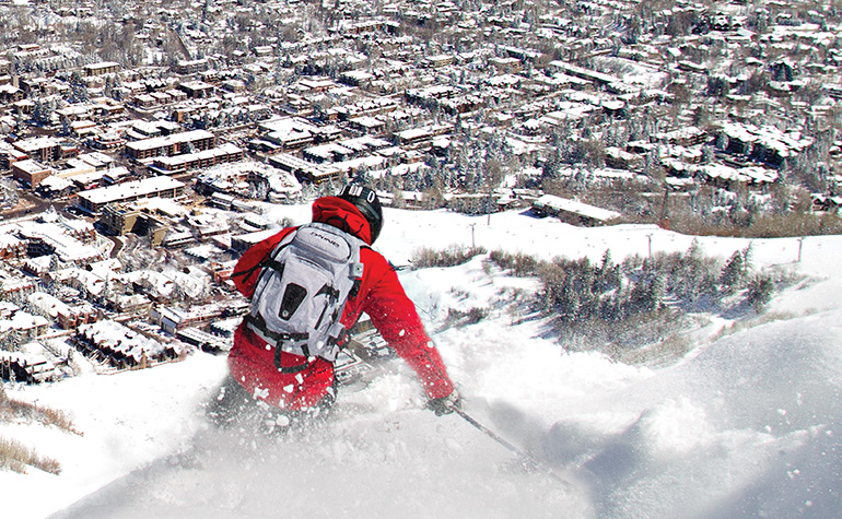 A man skis down a mountain towards downtown Aspen.